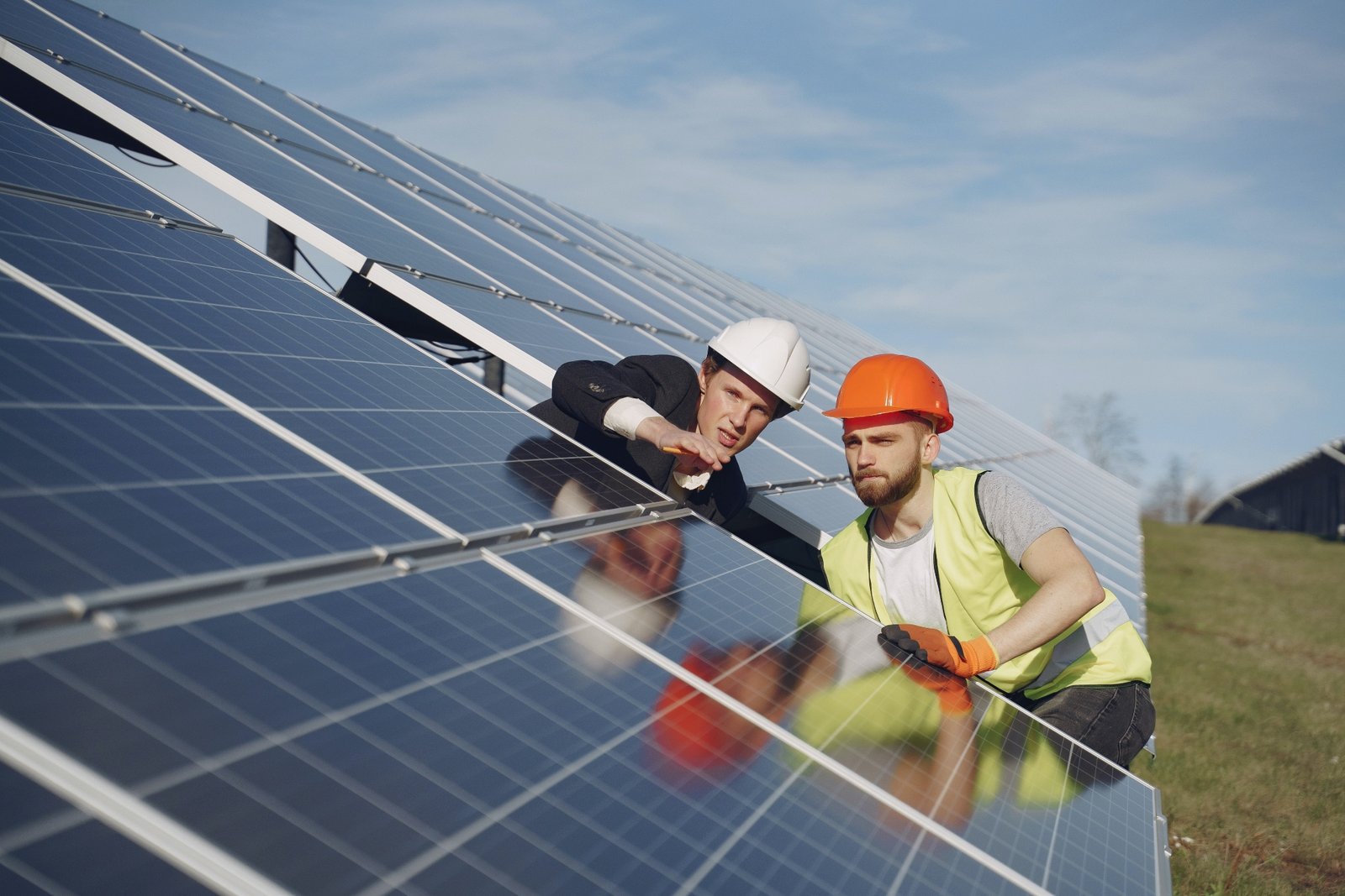 Two men in hard hats examine a large solar panel in an outdoor field