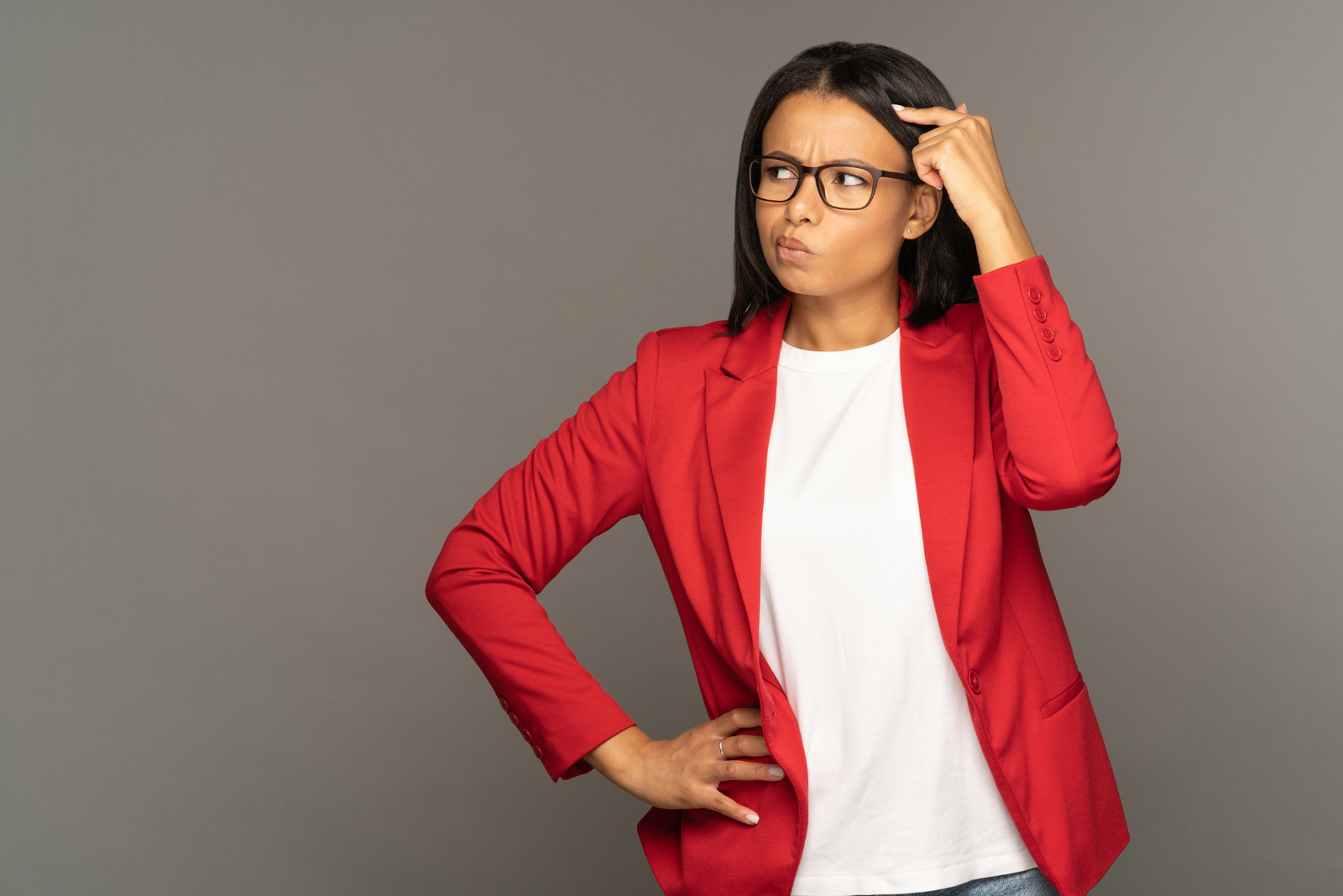 Woman wearing square glasses and red blazer scratches her head looking confused